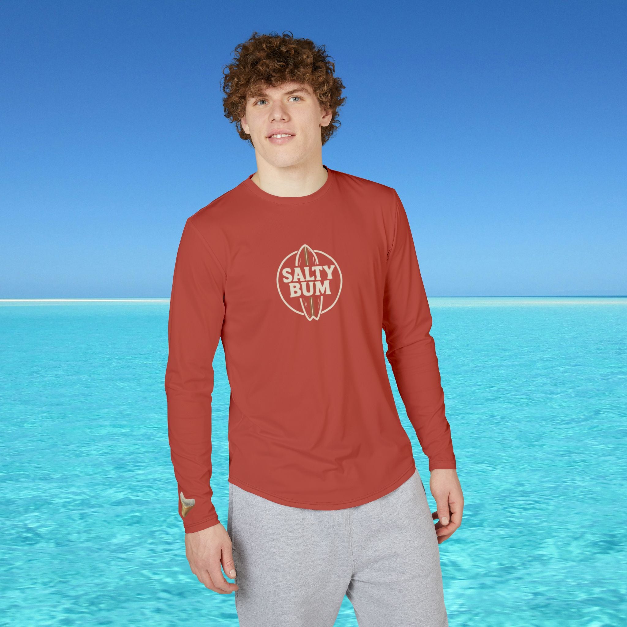 Person wearing a red 'Salty Bum' shirt standing in front of clear blue water and sky.