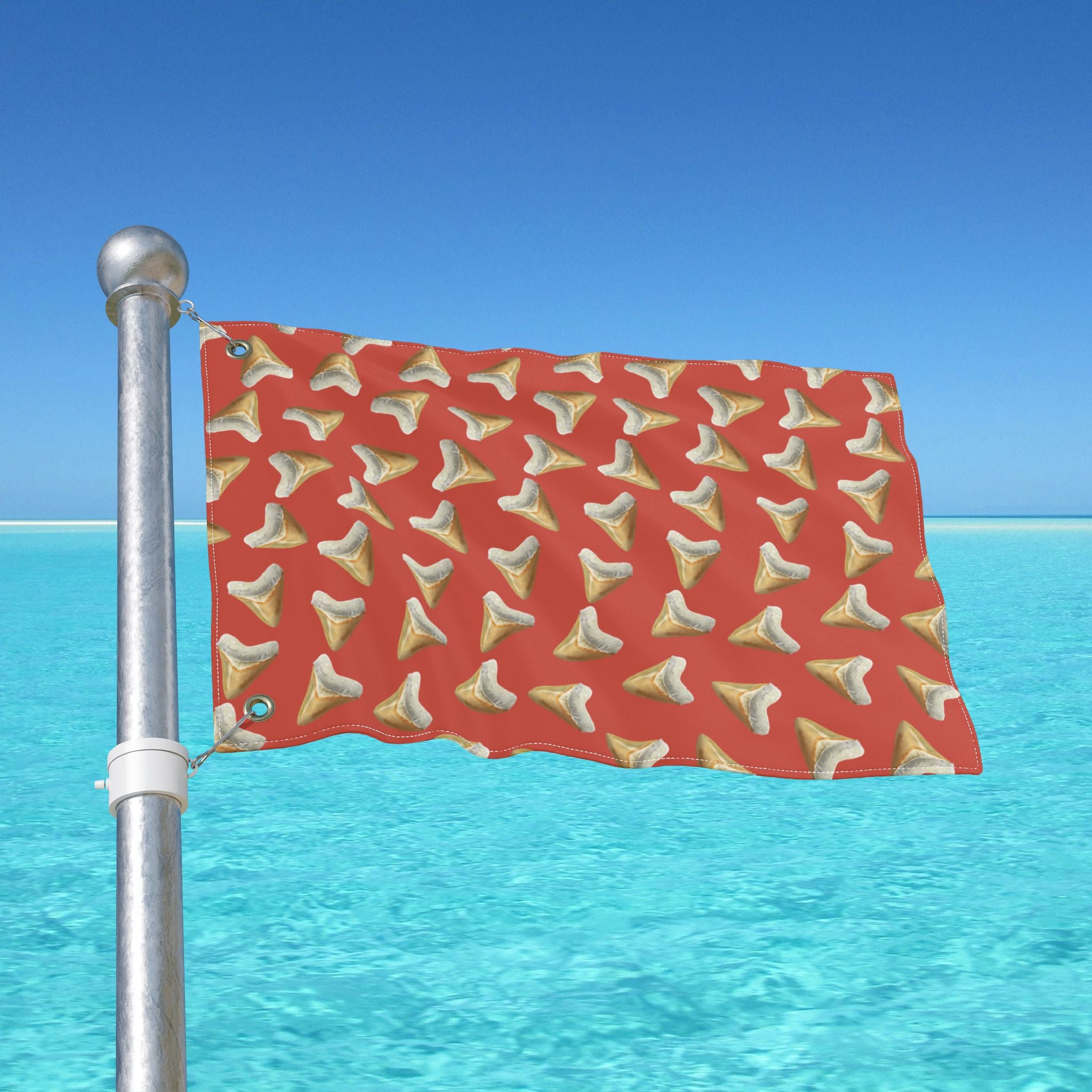 Red flag with shark tooth pattern on a pole against a blue sky and ocean background