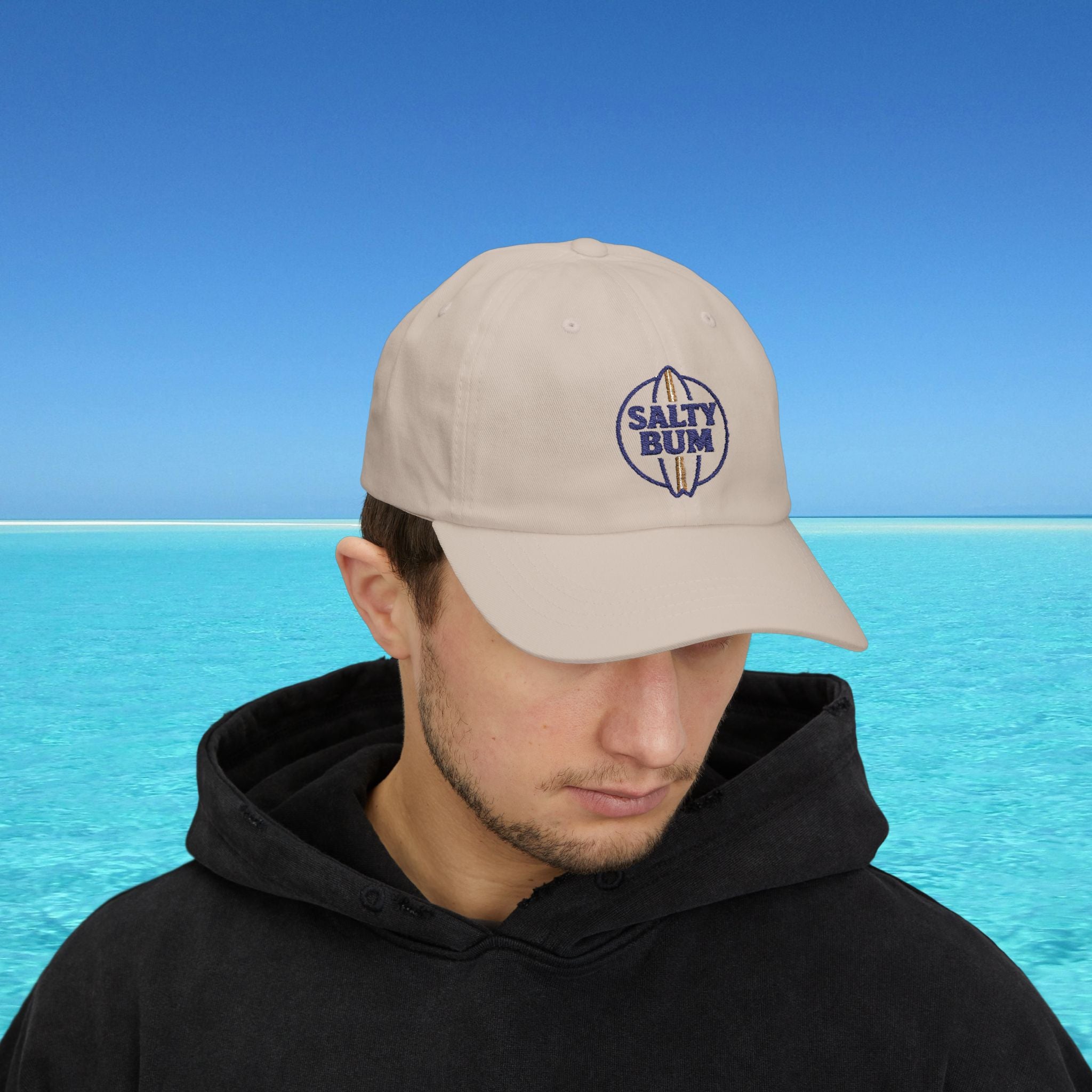 Man wearing a beige cap with 'Salty Bum' logo against a blue ocean background