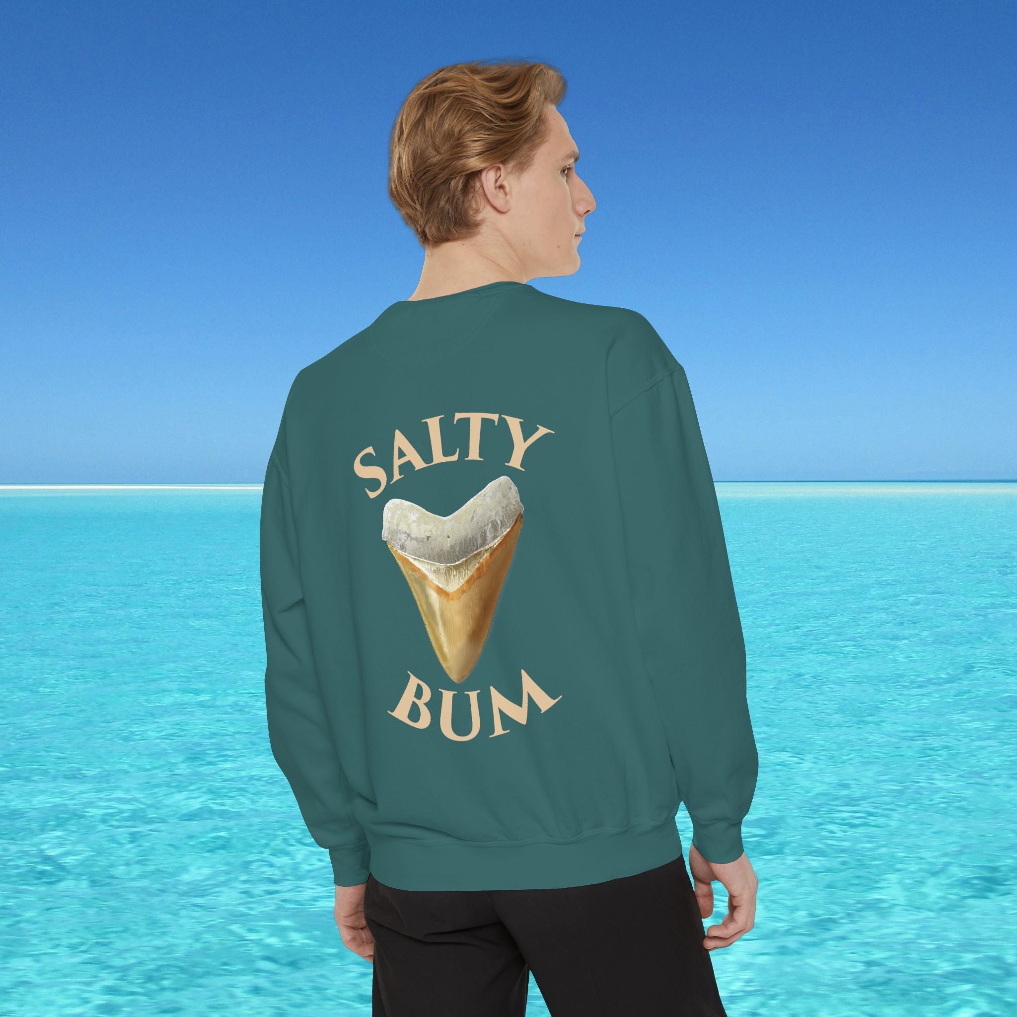 Person wearing a sweatshirt with 'Salty Bum' text and ice cream cone graphic, standing against a blue ocean background.