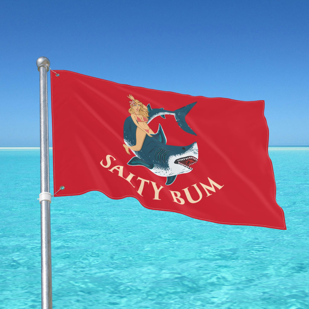 Red flag with 'Salty Bum' design against a clear blue sky and ocean.