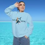 Person wearing a light blue sweatshirt with a graphic design and text, standing in front of a clear blue sky and ocean.