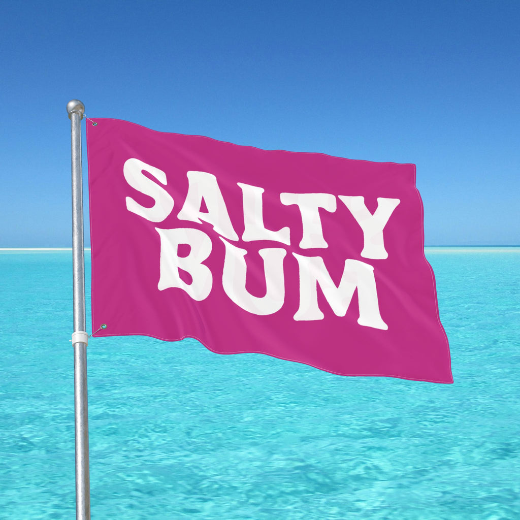 Pink flag with 'Salty Bum' text against a clear blue sky and ocean.