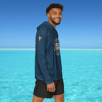 Man wearing a blue hoodie with 'Salt Bae' logo standing in front of clear blue water and sky.