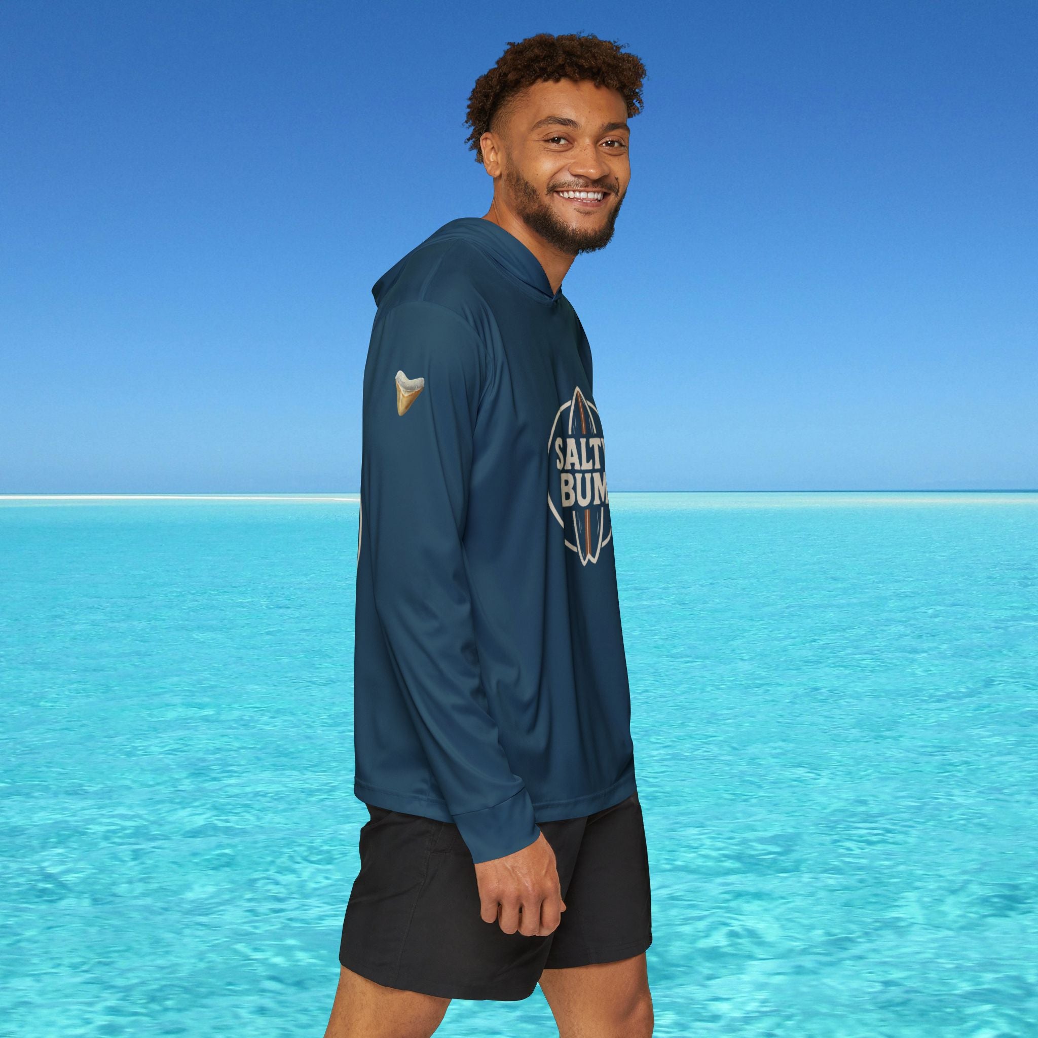 Man wearing a blue hoodie with 'Salt Bae' logo standing in front of clear blue water and sky.