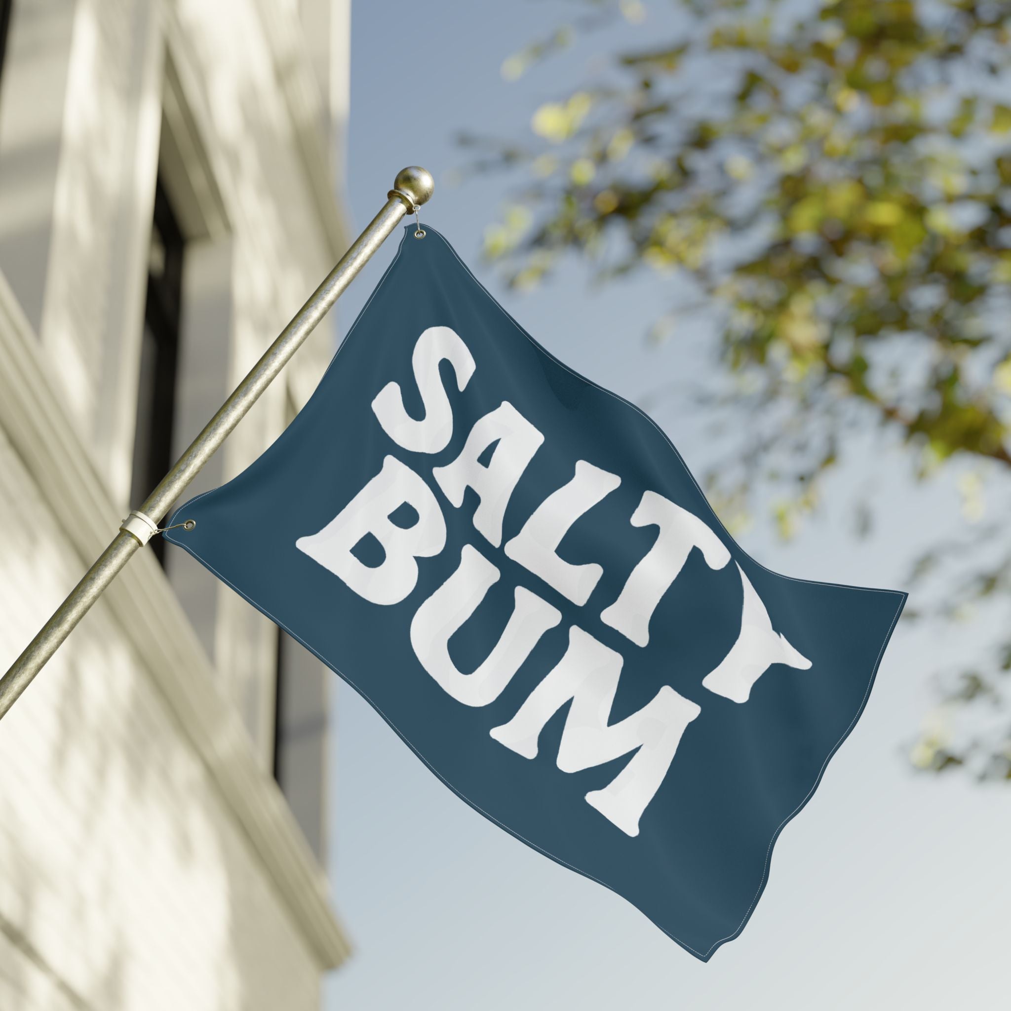 Flag with 'Salty Bum' text waving in front of a building and tree.