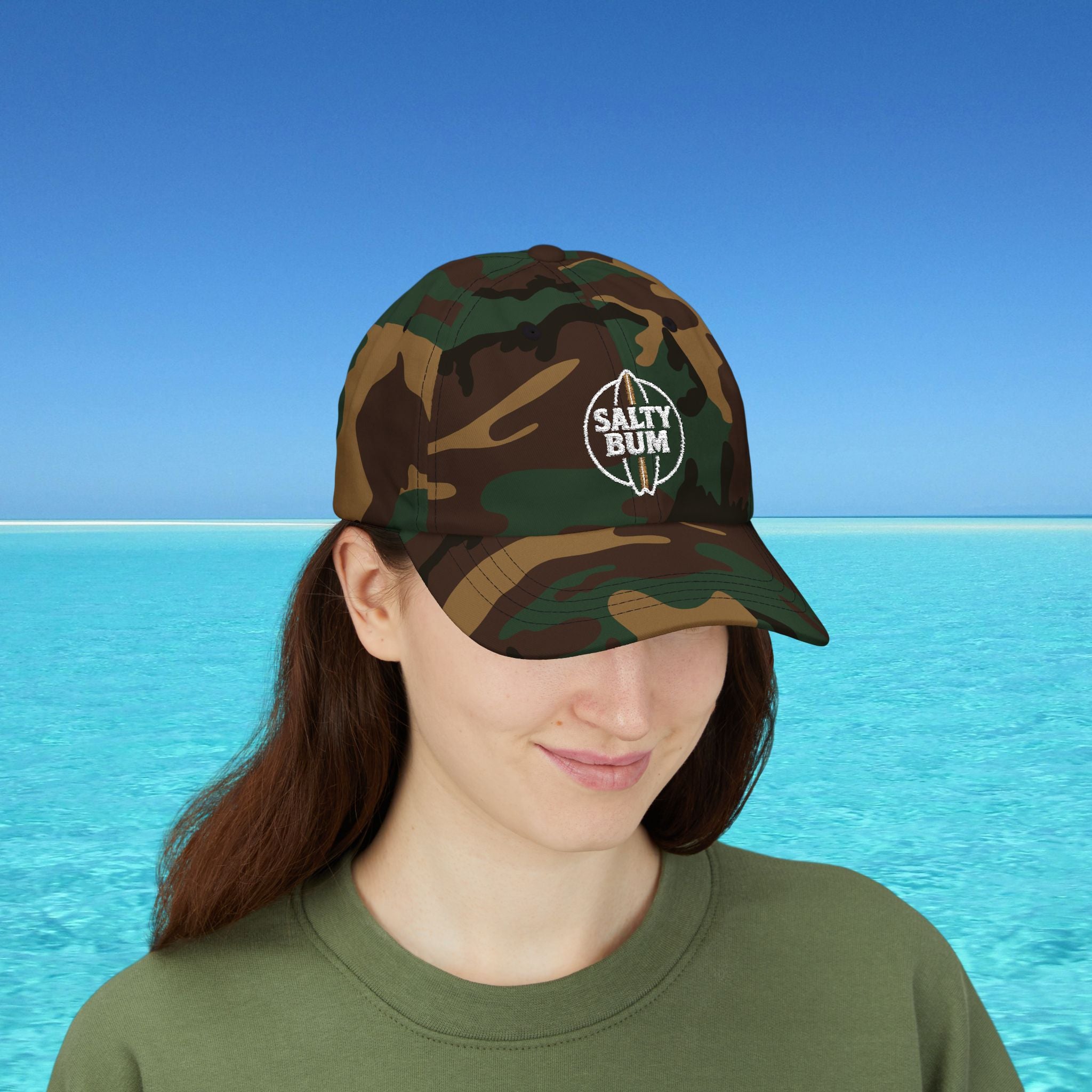 Person wearing a camouflage cap with 'Salty Bum' logo against a blue water and sky background
