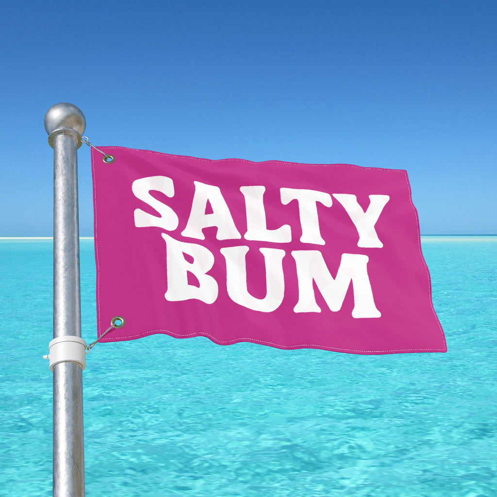 Pink flag with 'Salty Bum' text against a clear blue sky and ocean.