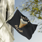 Black flag with a shark tooth graphic and 'Salty Bum' text, waving against a building and tree.