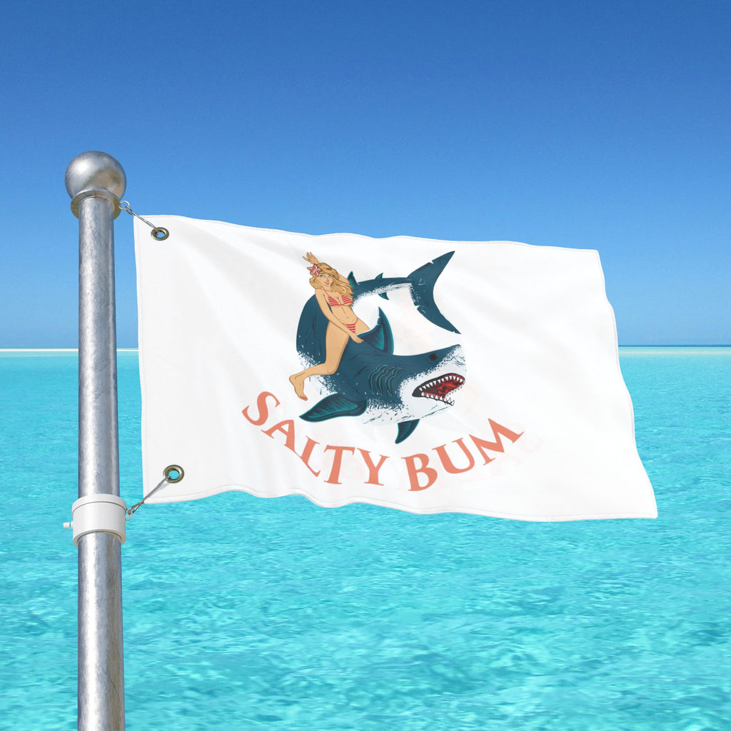 Flag with a shark and mermaid design on a pole over blue water and sky