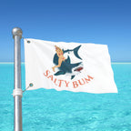 Flag with a shark and mermaid design on a pole over blue water and sky