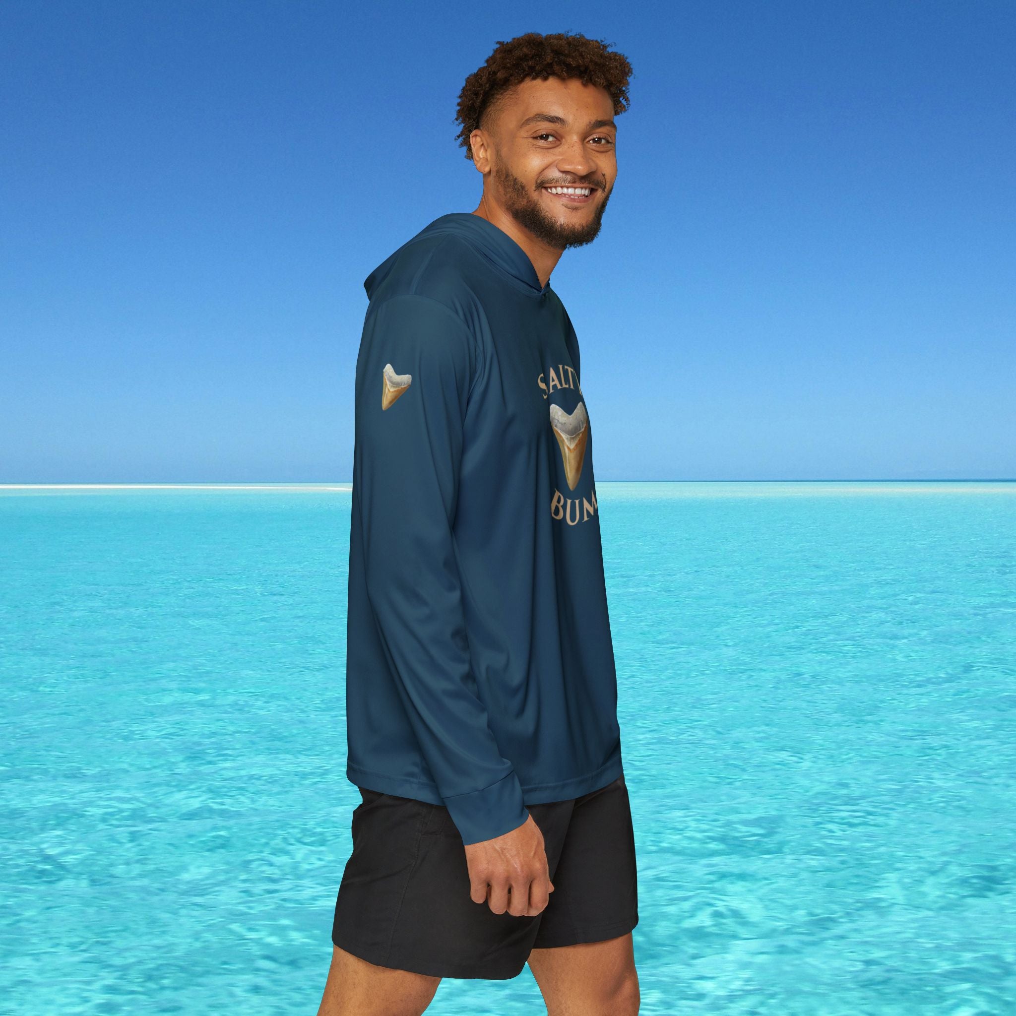 Man wearing a blue hoodie with a logo standing in front of clear blue water and sky.