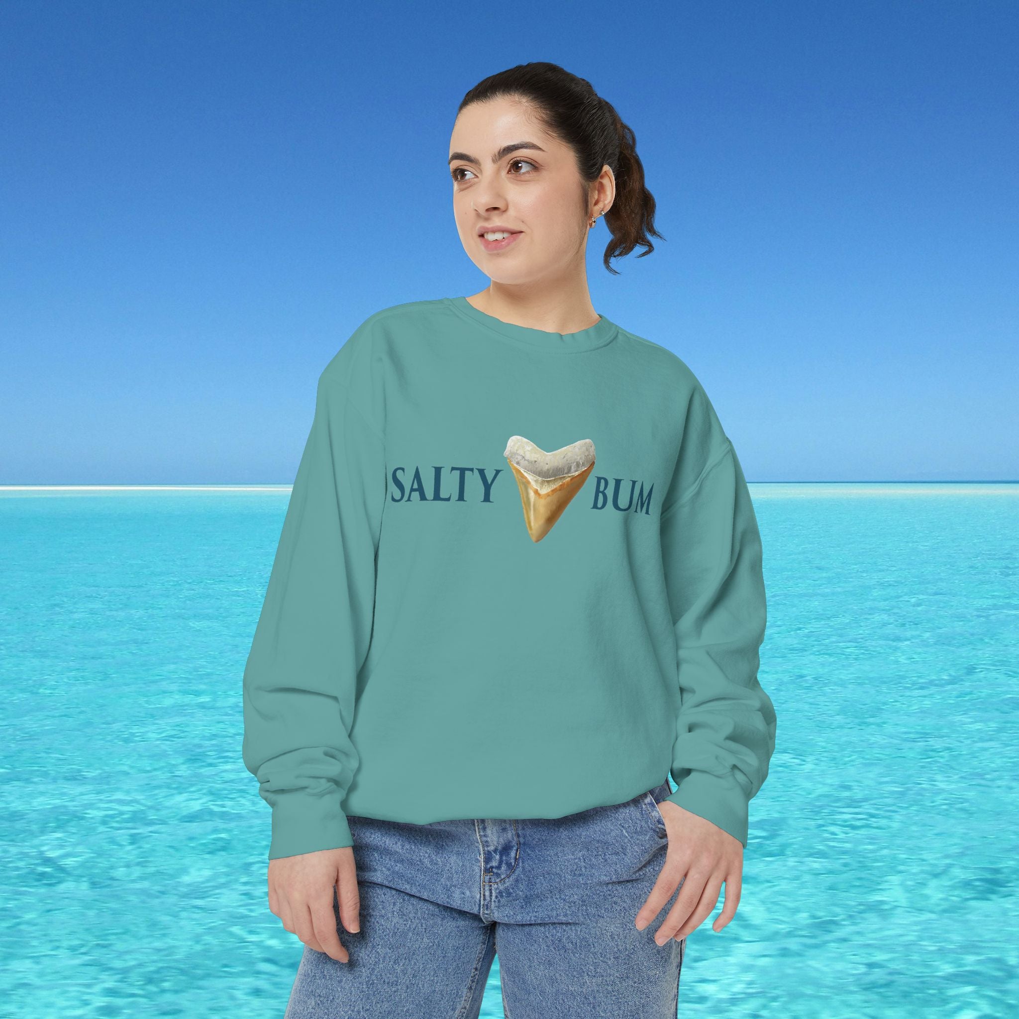Person wearing a teal sweatshirt with 'Salty Bum' text and ice cream graphic against a blue ocean background