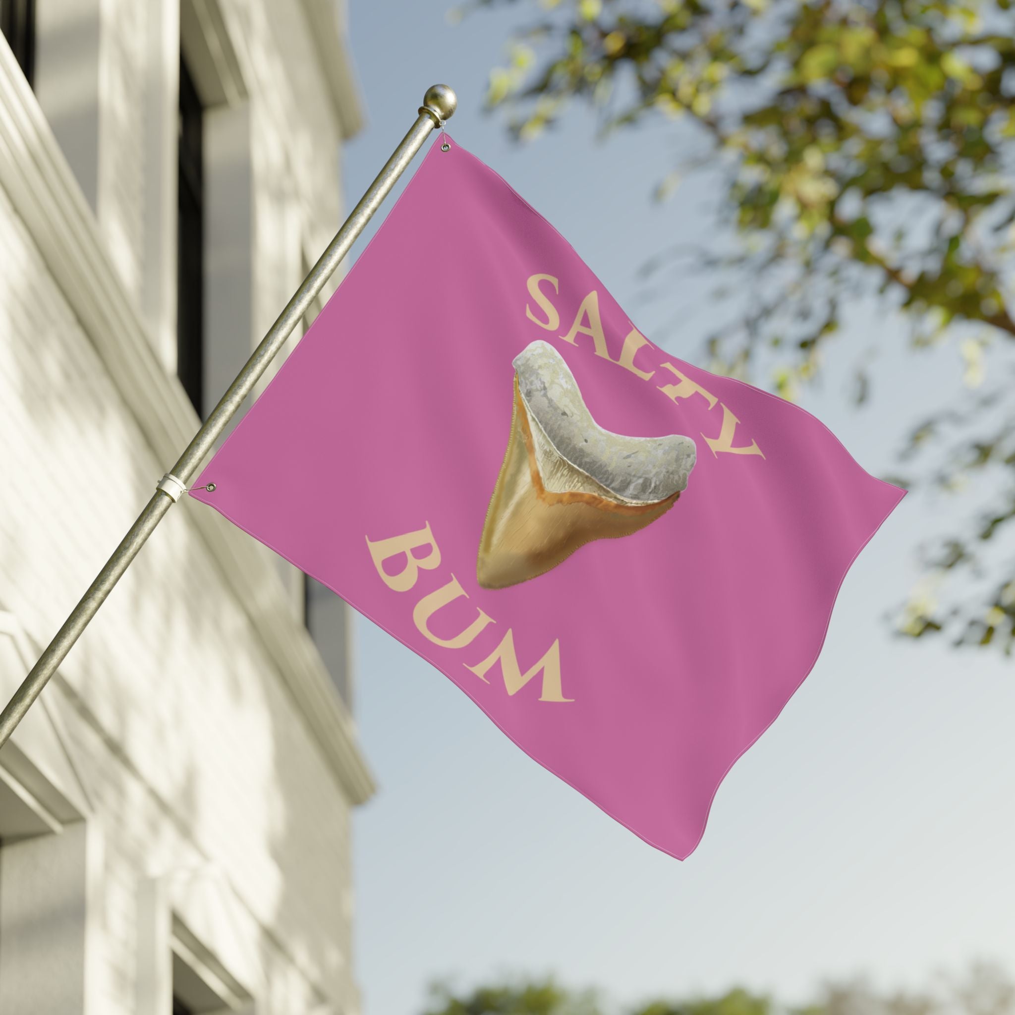 Flag with a shark tooth graphic and 'Salty Bum' text on a pink background, waving in front of a building.
