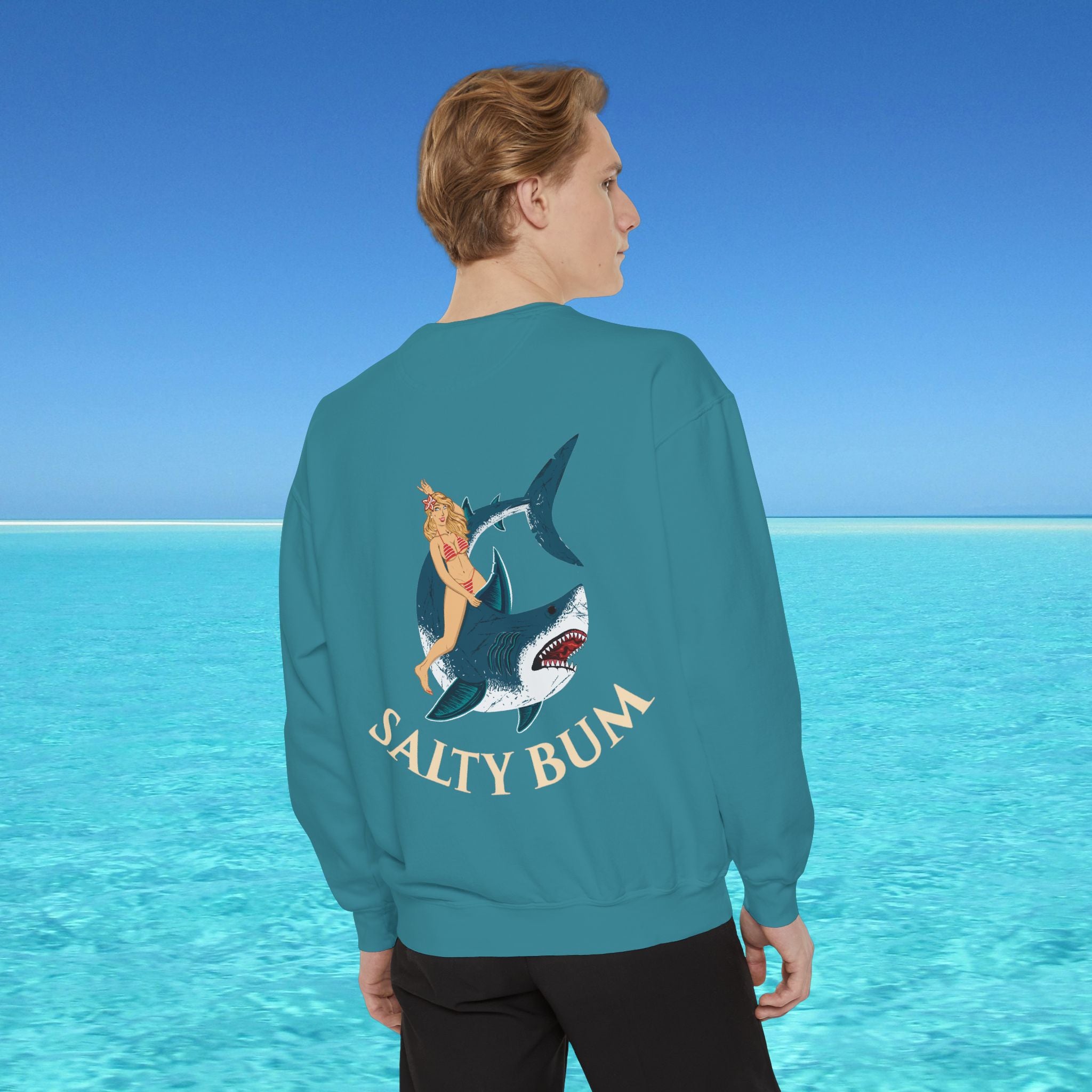 Person wearing a teal sweatshirt with a shark and bikini graphic and 'Salty Bum' text, standing in front of a blue ocean.
