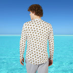 Man wearing a patterned shirt standing on a beach with clear blue water and sky.