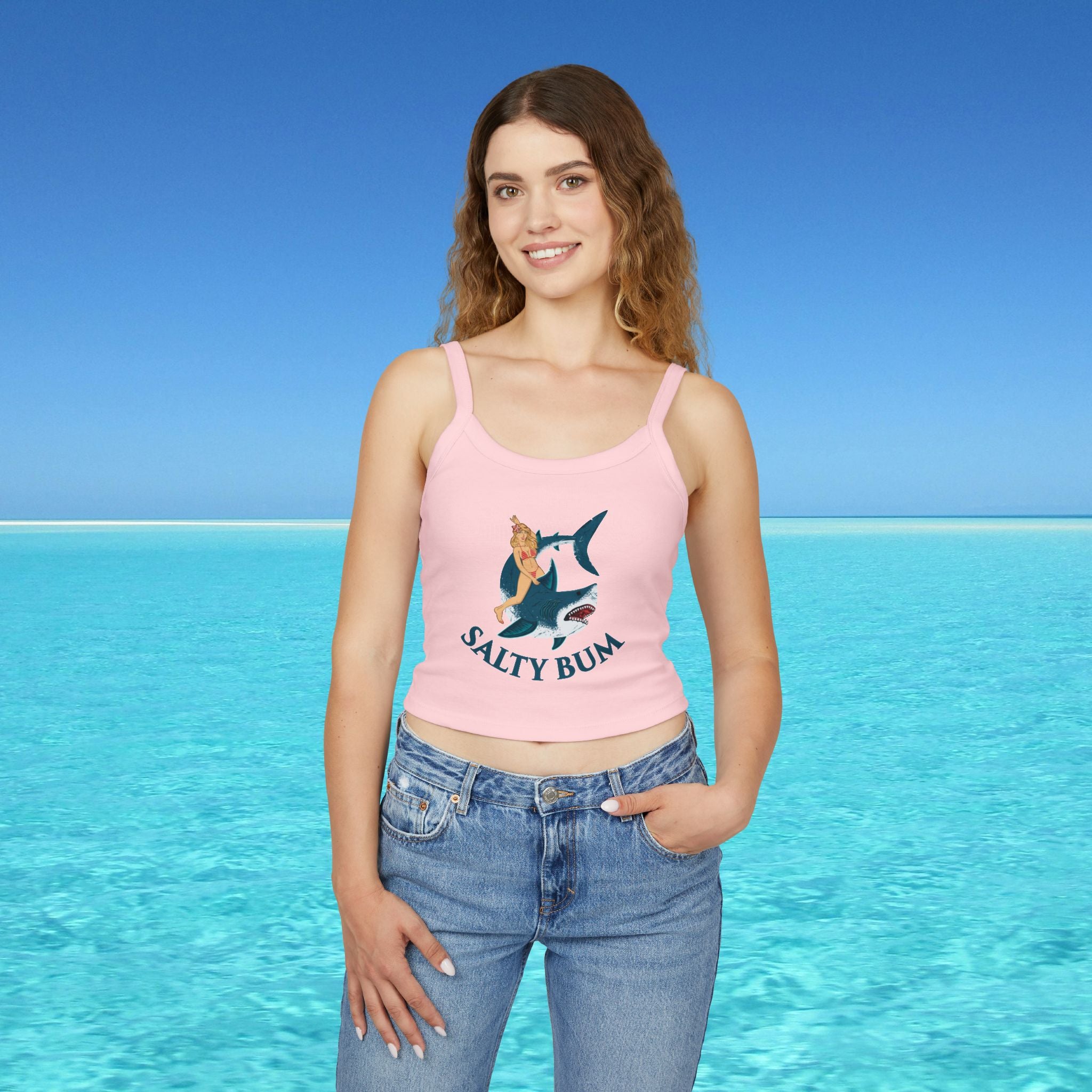 Woman wearing a pink tank top with a shark graphic and 'Salty Bum' text, standing in front of a clear blue ocean.