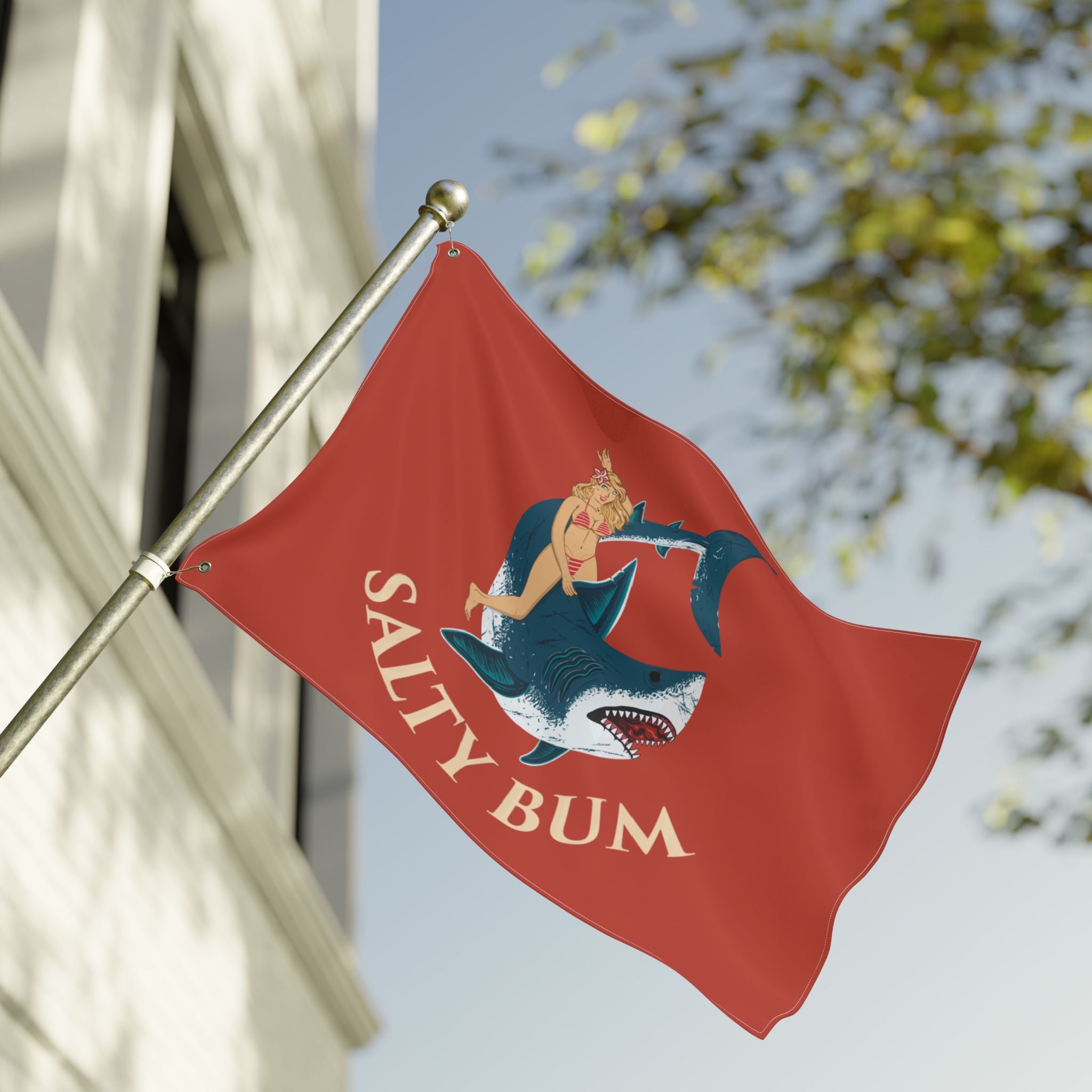 Red flag with a shark and bikini-clad woman design, featuring 'Salty Bum' text, against a blurred outdoor background.