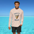 Man wearing a 'Salty Bum' hoodie with a shark tooth graphic against a clear blue sky and ocean.