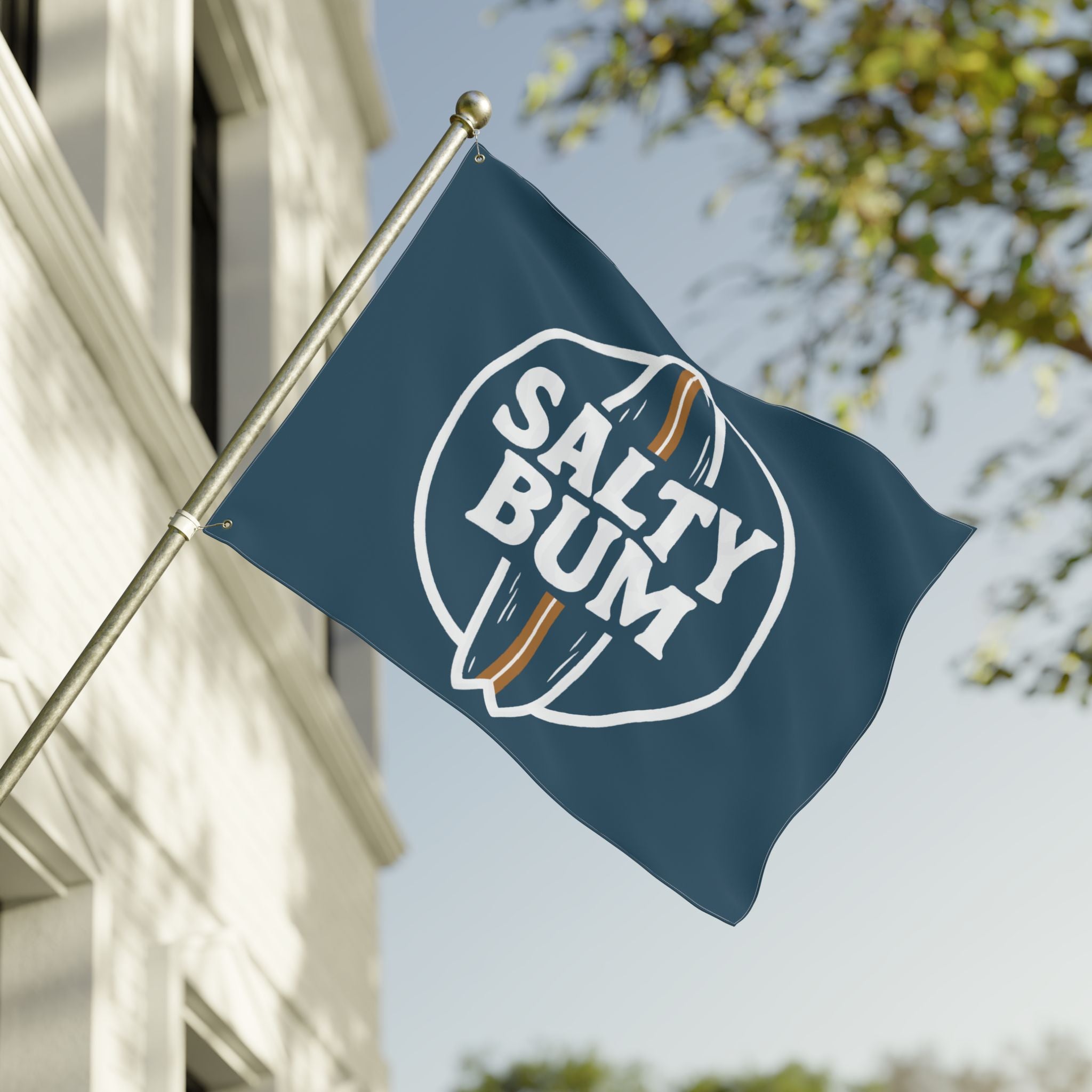 Flag with 'Salty Bum' logo waving in front of a building with trees in the background
