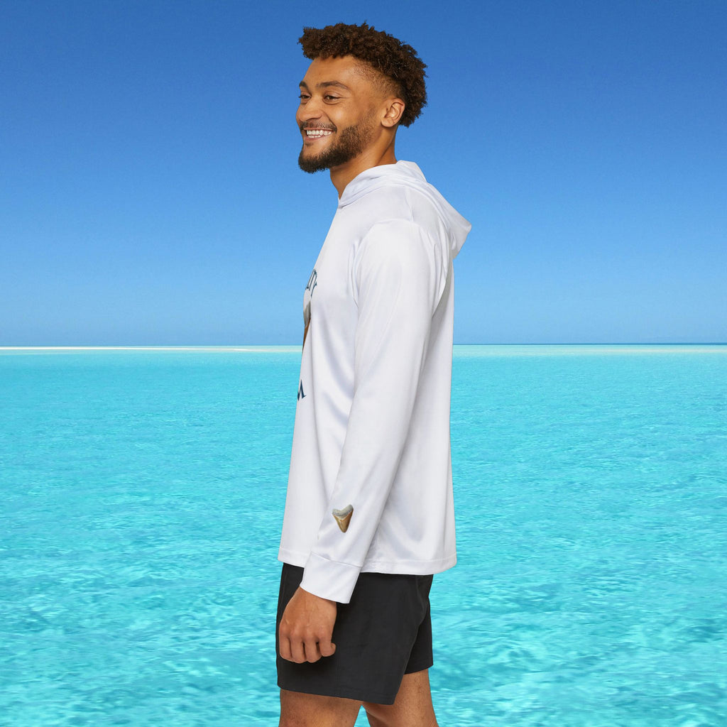 Man standing by clear blue water wearing a white long-sleeve shirt and black shorts.