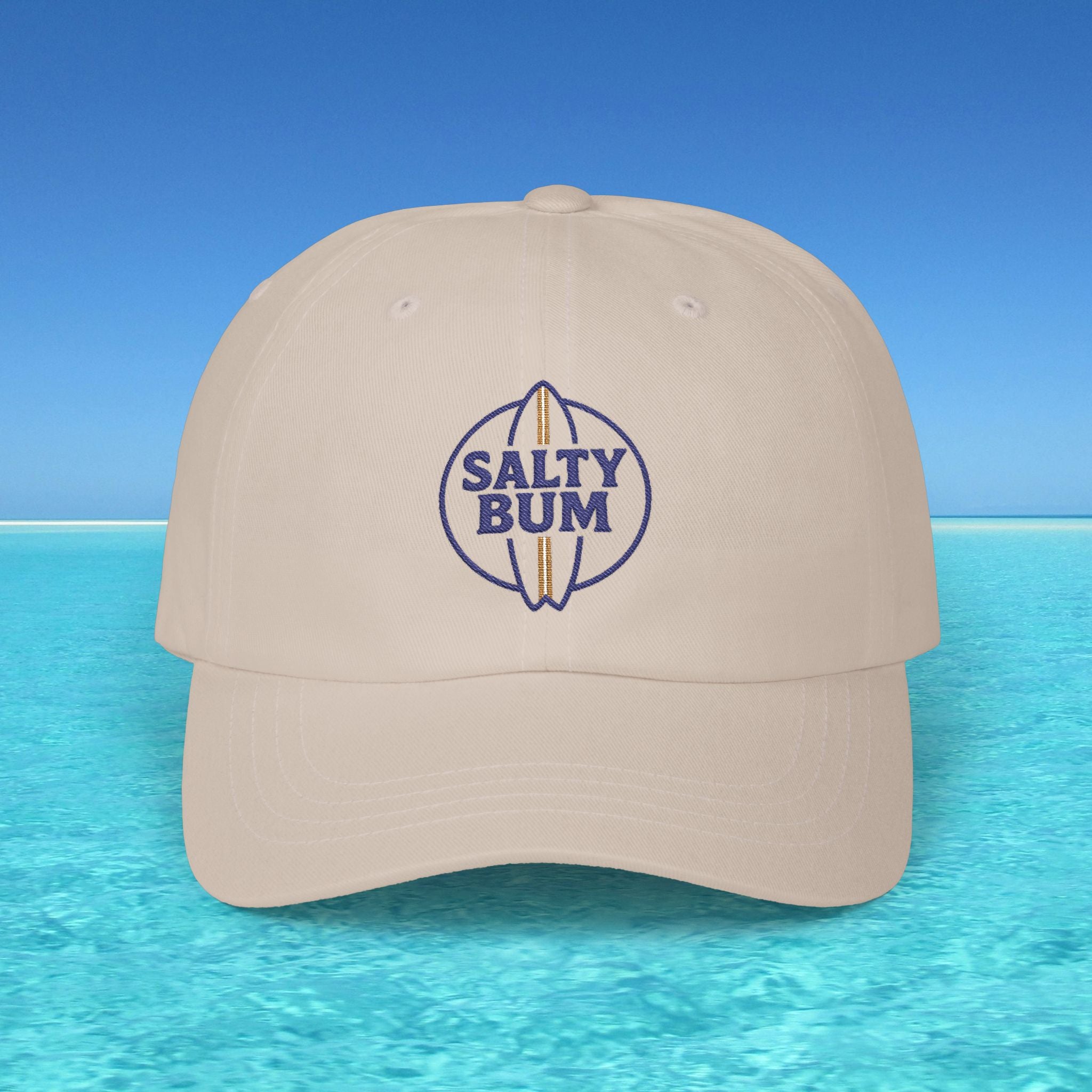 Beige cap with 'Salty Bum' logo on a blue water and sky background