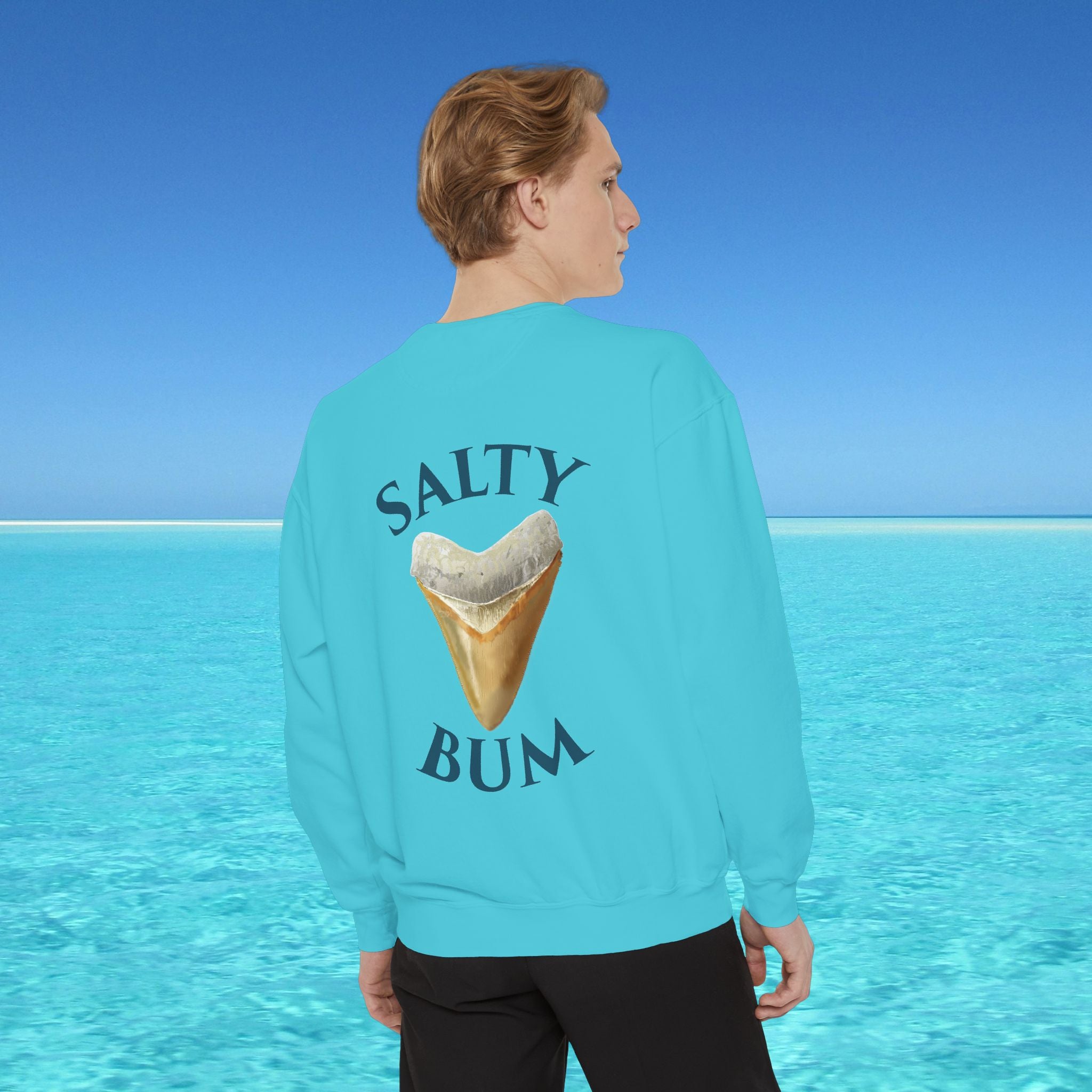 Person wearing a turquoise sweatshirt with 'Salty Bum' text and ice cream graphic, standing in front of a clear blue ocean.