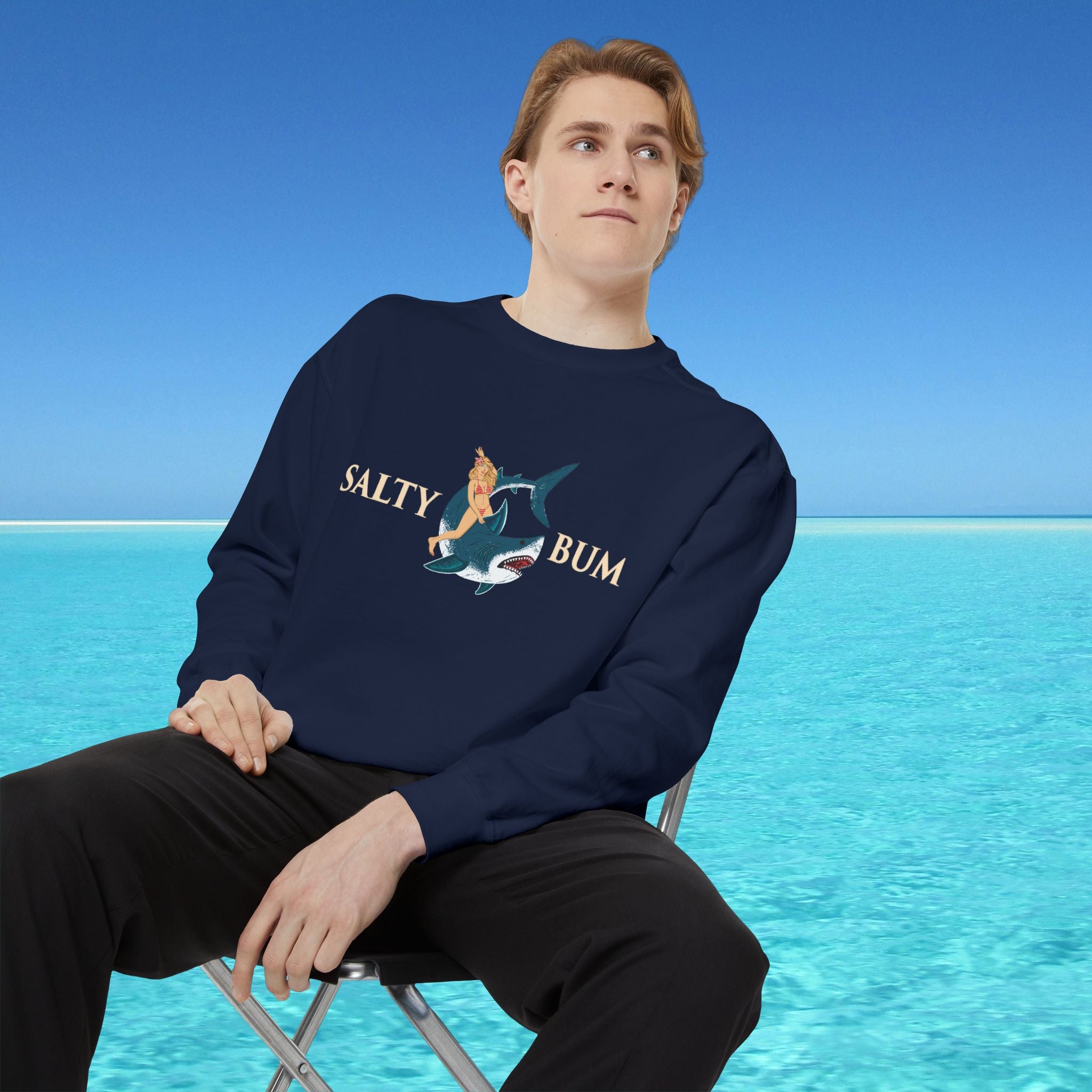 Person wearing a navy blue sweatshirt with 'Salty Bum' graphic sitting on a chair with a blue water and sky background.