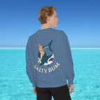 Person wearing a blue sweatshirt with a shark and bikini design, standing in front of a clear blue ocean.