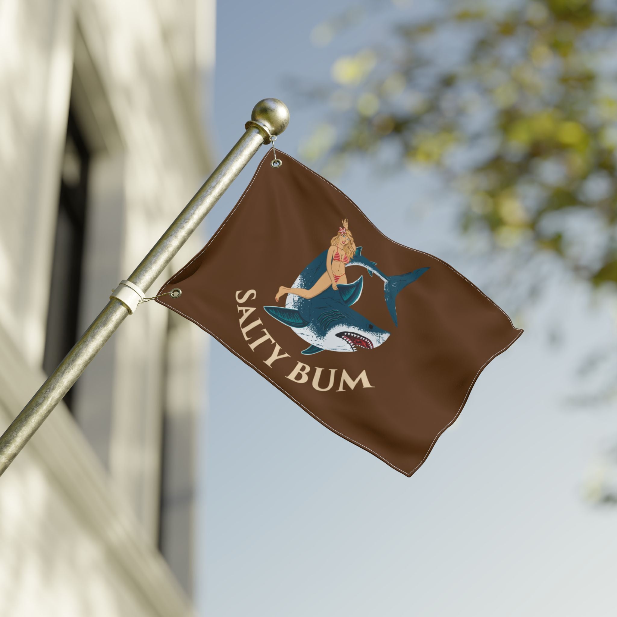 Brown flag with 'Salty Bum' design featuring a mermaid and shark, attached to a pole outdoors.