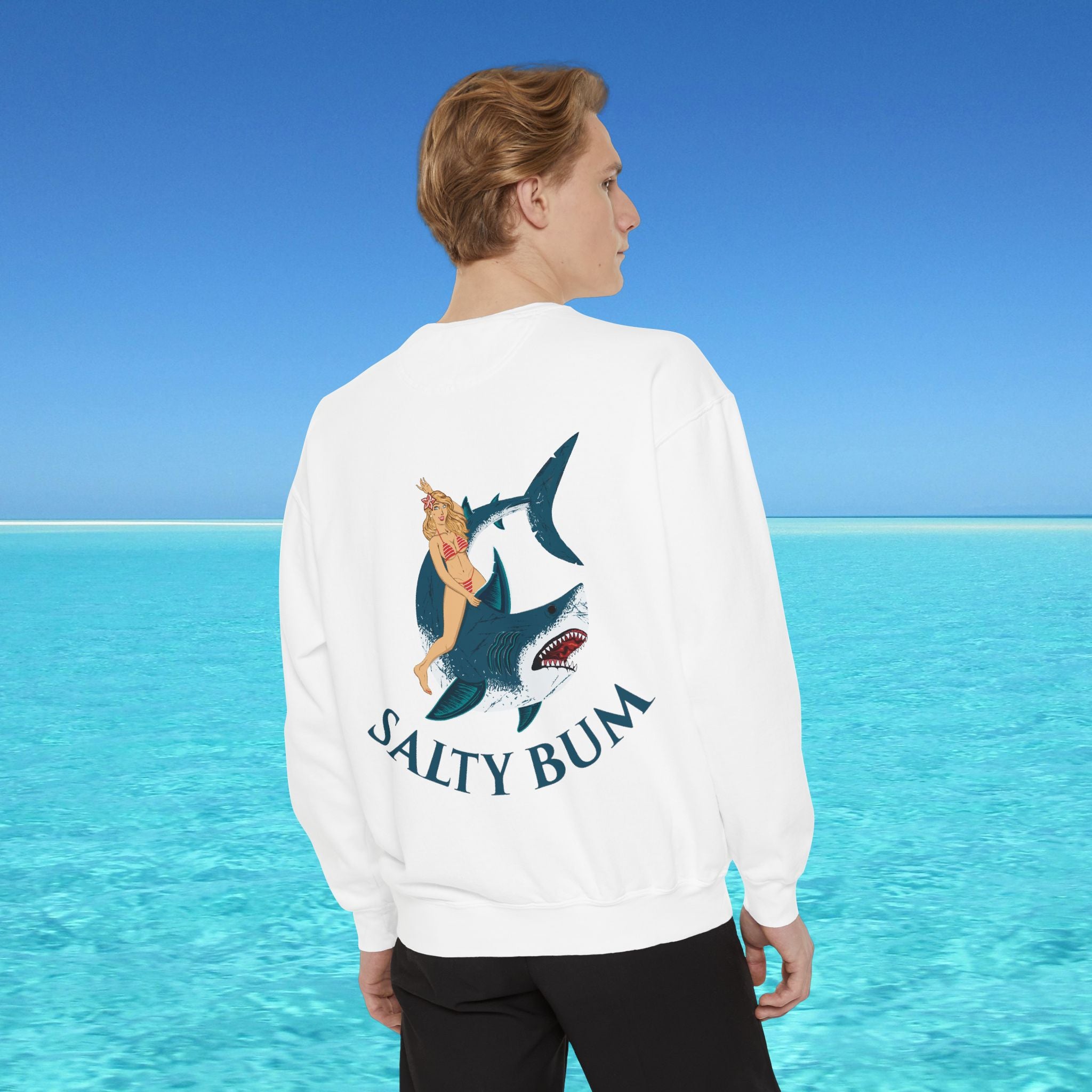 Person wearing a white sweatshirt with a shark graphic and 'Salty Bum' text, standing in front of a blue ocean.