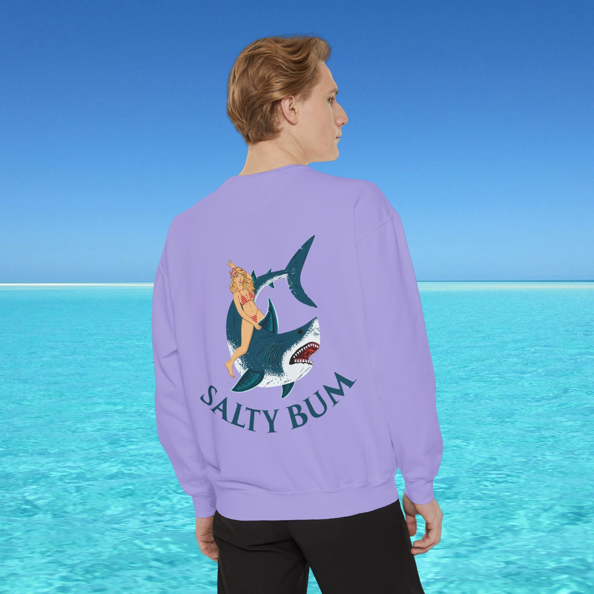 Person wearing a purple sweatshirt with a shark and mermaid design and 'Salty Bum' text, standing in front of a blue ocean.