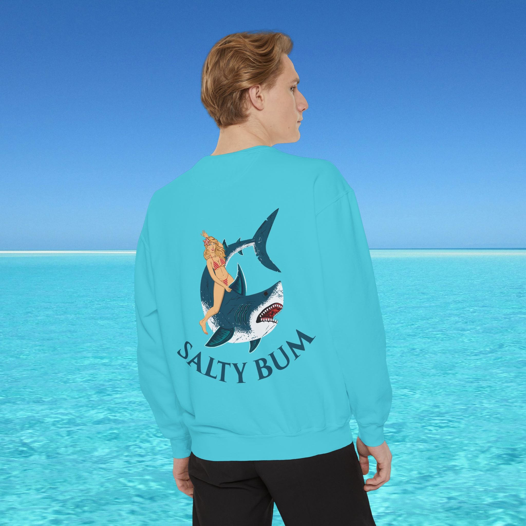 Person wearing a turquoise sweatshirt with a shark and bikini graphic and 'Salty Bum' text, standing in front of a blue ocean.