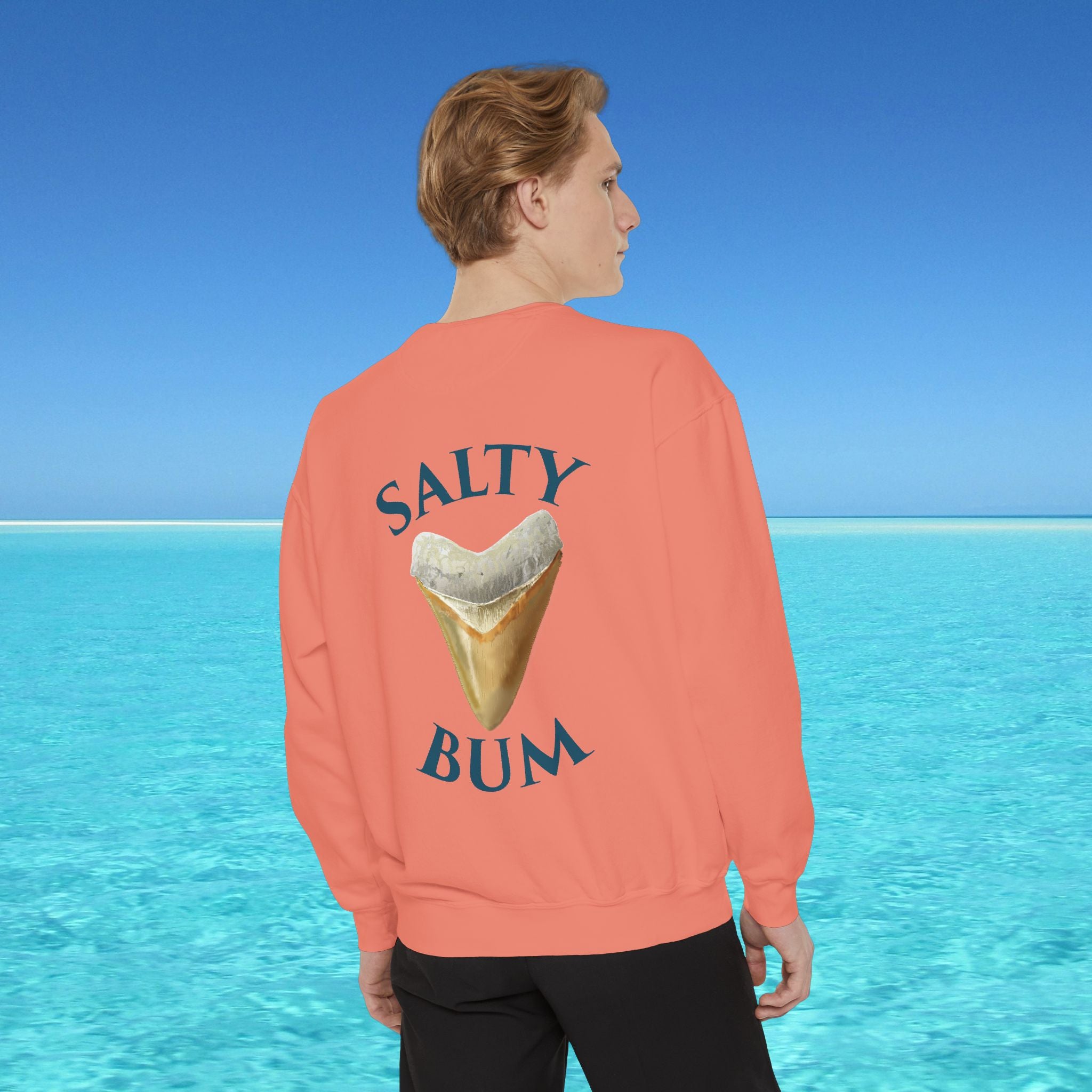 Person wearing a coral sweatshirt with 'Salty Bum' text and ice cream graphic, standing against a blue ocean background.
