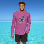 Man wearing a purple long-sleeve shirt with a graphic design and text, standing in front of clear blue water.