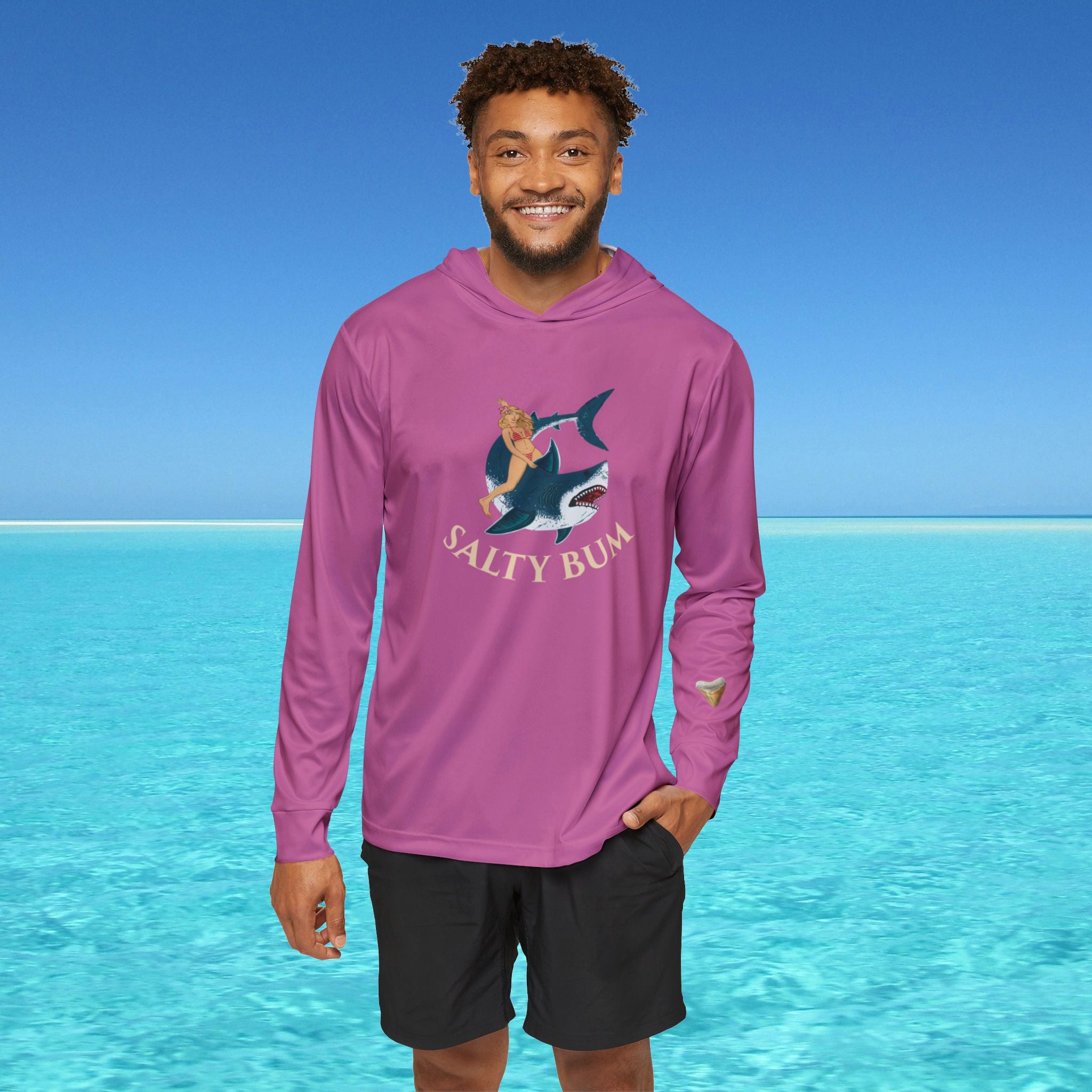 Man wearing a purple long-sleeve shirt with a graphic design and text, standing in front of clear blue water.