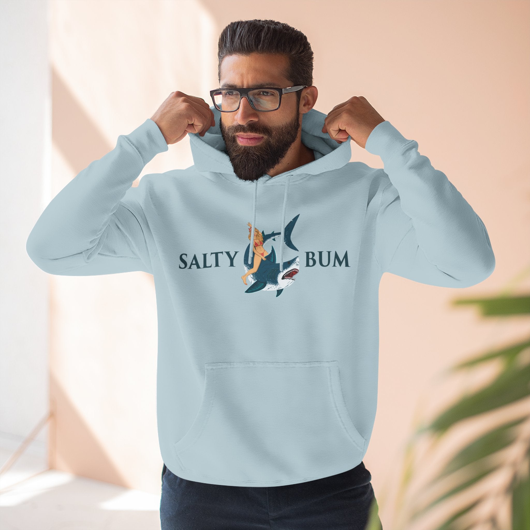 Man wearing a light blue hoodie with 'Salty Bum' logo, flexing muscles indoors.