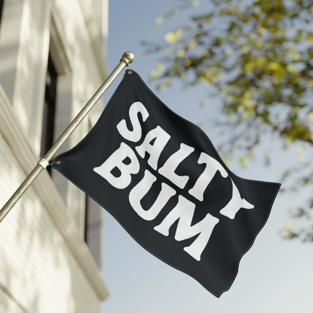 Black flag with 'Salty Bum' text waving in front of a building and tree.