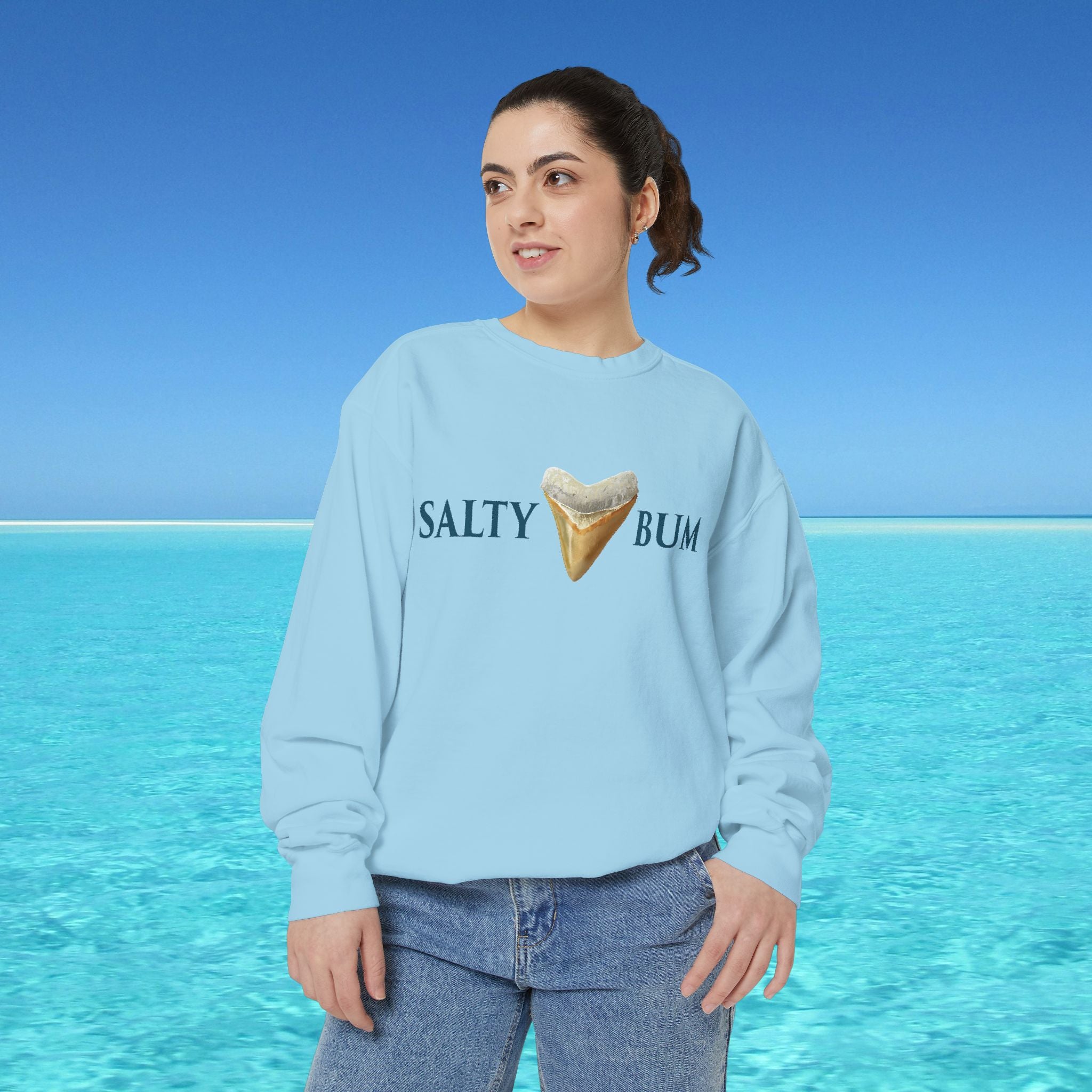 Person wearing a light blue sweatshirt with 'Salty Bum' text and ice cream graphic against a blue sky and ocean background.