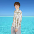 Person wearing a geometric patterned shirt standing in front of clear blue water and sky.