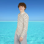 Person wearing a geometric patterned shirt standing in front of clear blue water and sky.