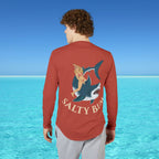 Person wearing a red long-sleeve shirt with a shark and mermaid graphic and 'Salty Bum' text, standing in front of clear blue water.