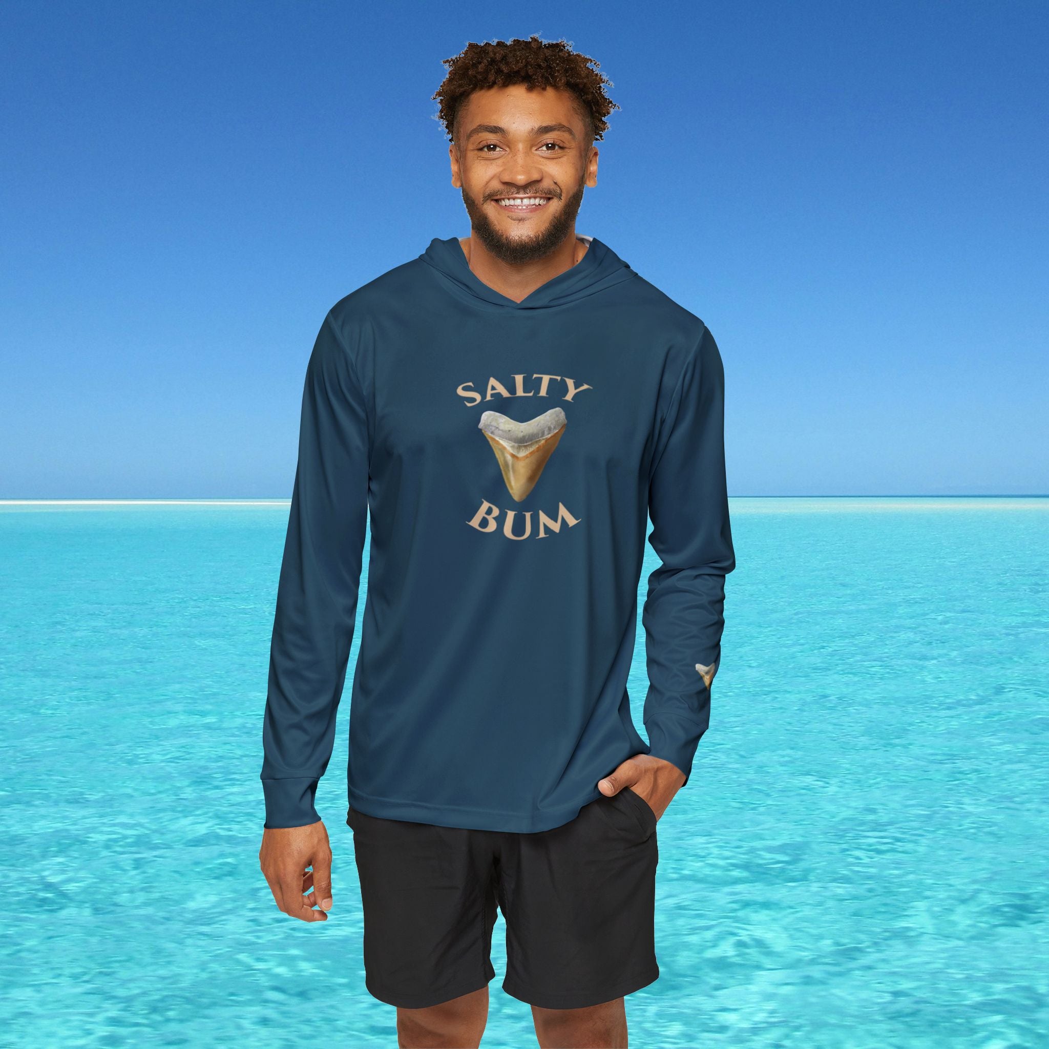 Man wearing a blue hoodie with 'Salty Bum' text and graphic, standing in front of clear blue water.