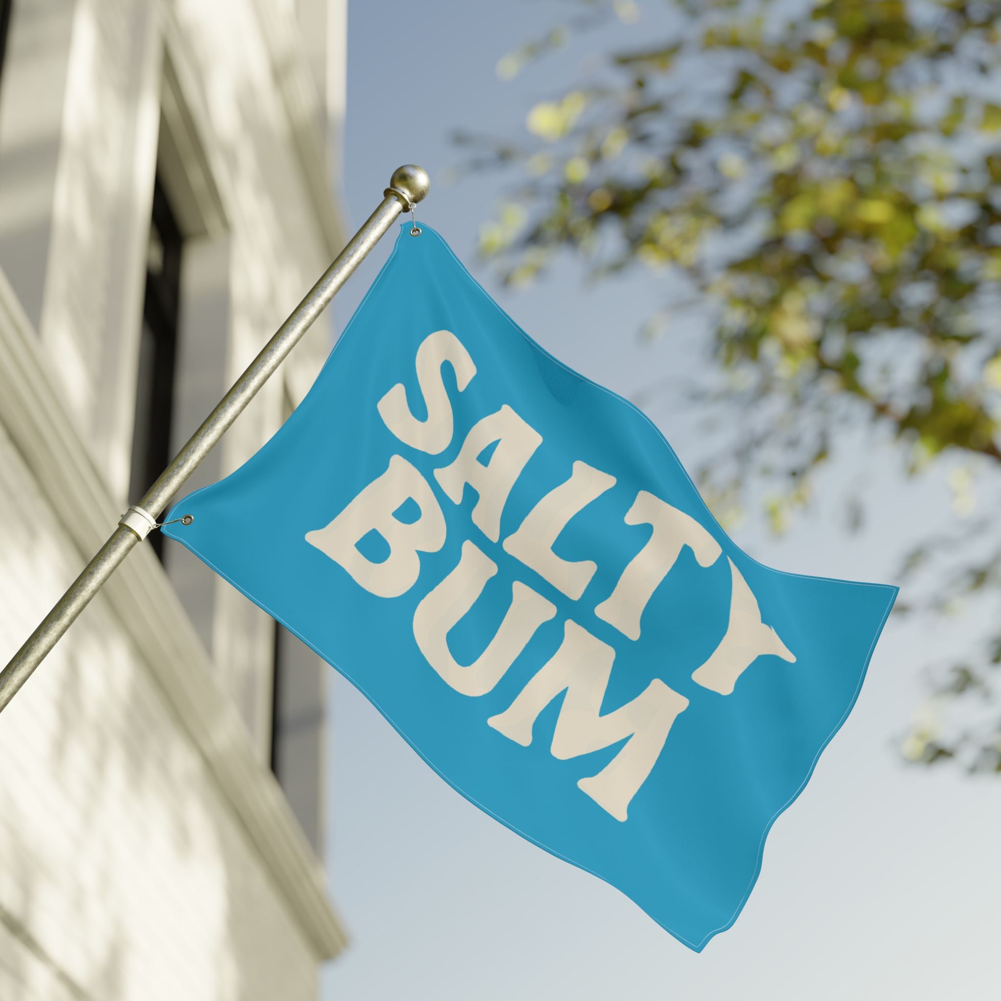 Blue flag with 'Salty Bum' text on a building facade with trees in the background