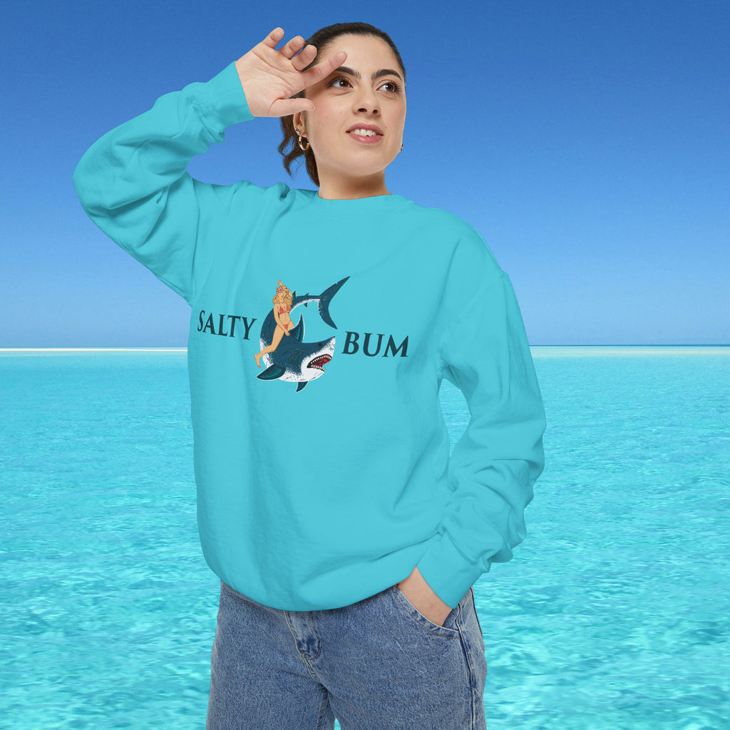 Person wearing a turquoise sweatshirt with a graphic design and text, standing in front of a clear blue sky and ocean.