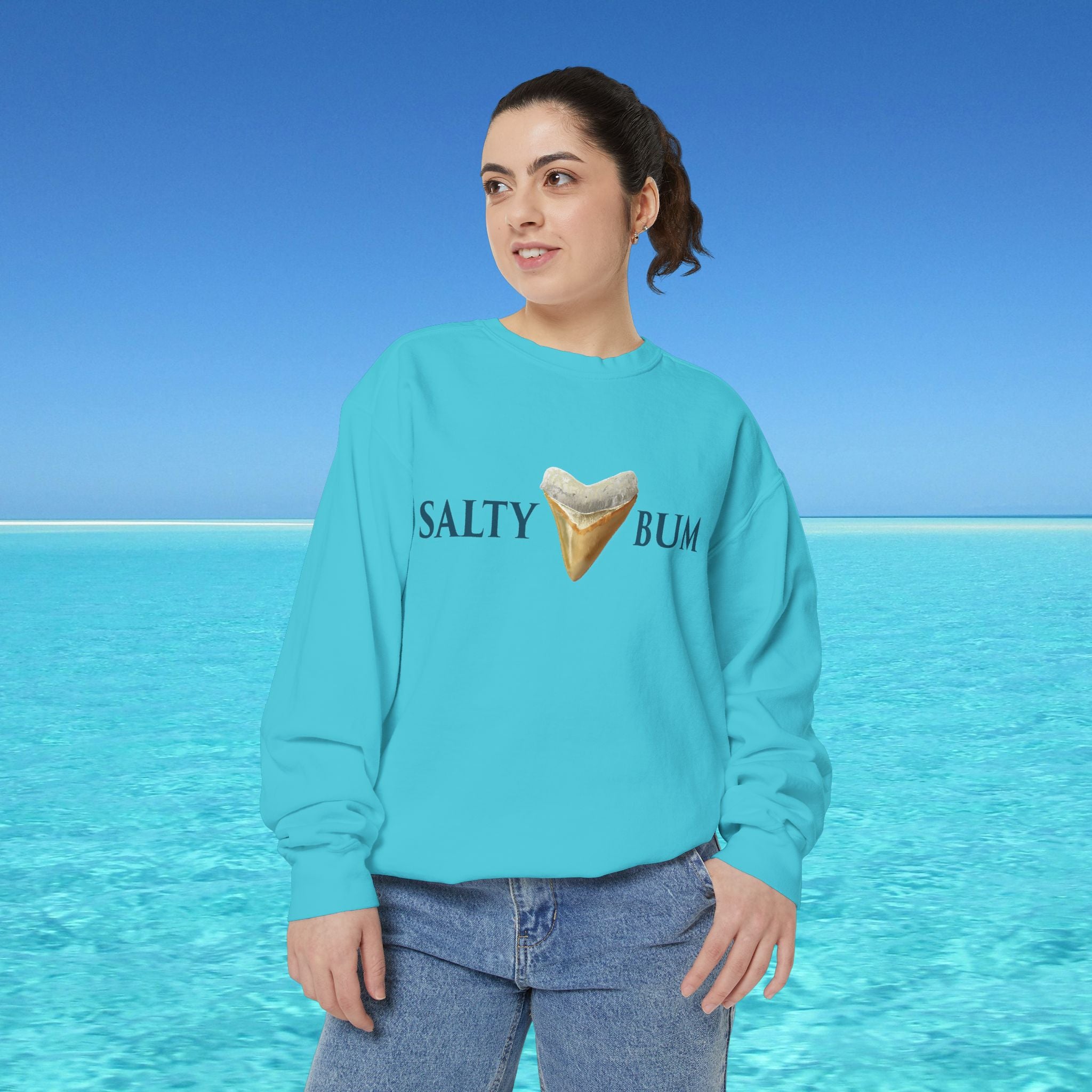 Person wearing a turquoise sweatshirt with 'Salty Bum' text and ice cream graphic against a blue ocean background