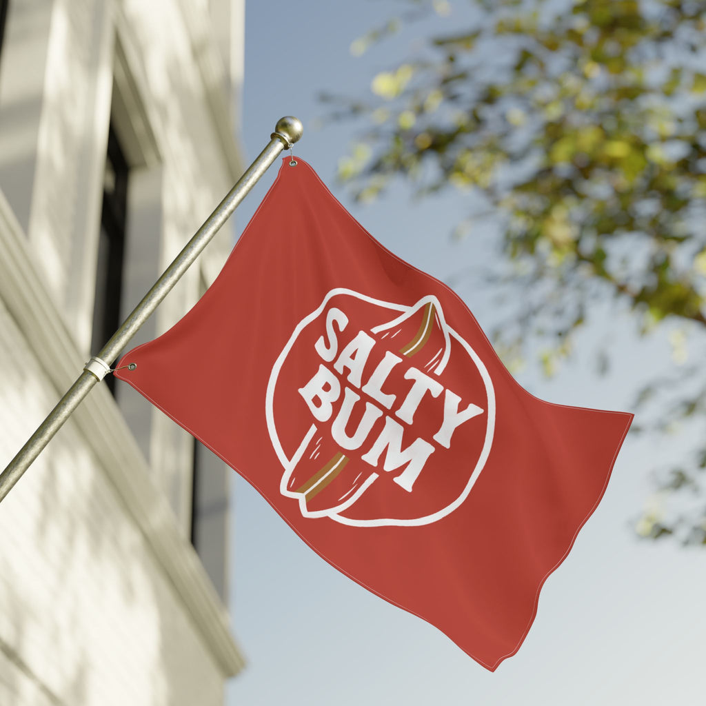 Red flag with 'Salty Bum' logo on a building facade with trees in the background