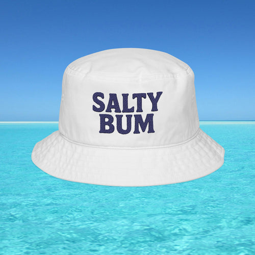 White bucket hat with 'Salty Bum' text floating on clear blue water with a blue sky background