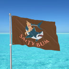 Flag with shark and bikini illustration on a pole against a blue sky and water background