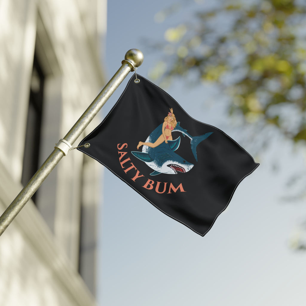 Flag with a shark and bikini-clad figure design, featuring the text 'Salty Bum', waving on a flagpole against a blurred background.